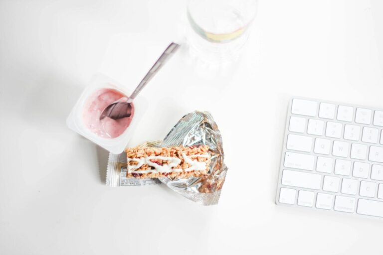 A stylish flat lay of yogurt and granola bar on a desk, perfect for a quick healthy snack.