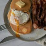 A delectable breakfast featuring pancakes, poached egg, and crispy bacon on a plate.